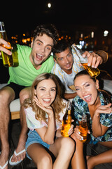 Selective focus of friends with beer bottles having fun outdoors at night