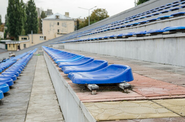 Lots of empty seats in the stadium. Texture of blue chairs. Plastic seats are arranged in a row. Dirty and scratched fan seats.Stadium after rain