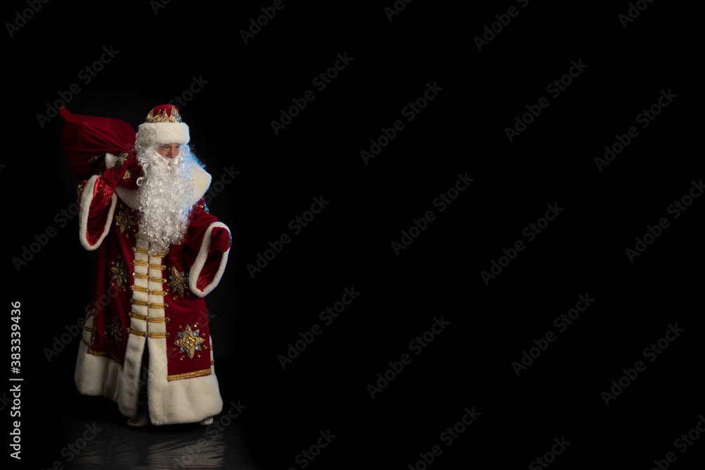 Wall mural Santa Claus in a red fur coat, with a white beard posing on a black background