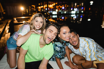 Excited young friends embracing and looking at camera at night