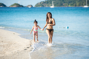 Fototapeta premium Asian family having fun running on a sandy beach. Happy asia family Having Fun In Sea On Beach Holiday. Mother and daughter happiness in bikini holding hand and running. people travel concept.