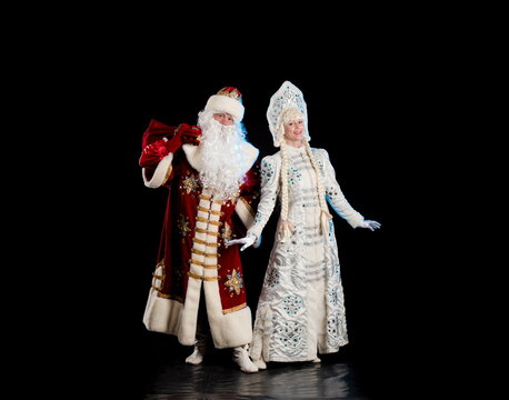 Santa Claus in a red suit and the Snow Maiden in a white fur coat posing against a black background