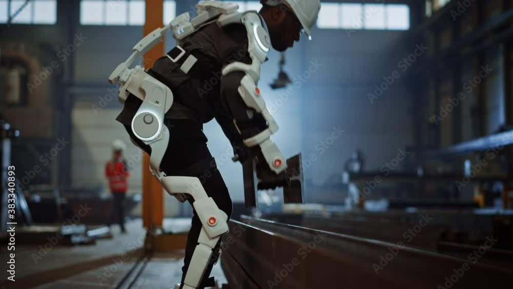 Poster Black African American Engineer is Testing a Futuristic Bionic Exoskeleton and Picking Up Metal Objects in a Heavy Steel Industry Factory
