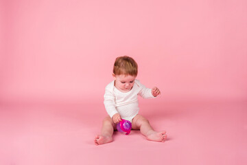 A little girl in a white bodysuit sits with a water bottle on a pink background with a copy of the space