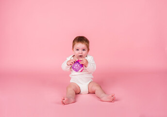 A little girl in a white bodysuit sits and drinks a bottle of water on a pink background with a copy of space
