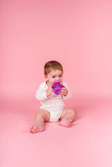 Portrait of a baby girl in a white bodysuit sitting and drinking a bottle of water on a pink isolated background with space for text