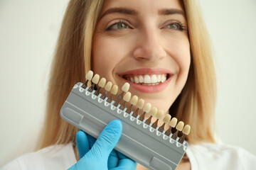 Doctor matching patient's teeth color with palette on white background, closeup. Cosmetic dentistry