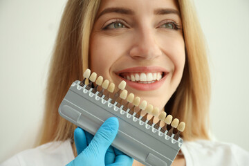 Doctor matching patient's teeth color with palette on white background, closeup. Cosmetic dentistry