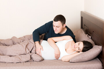 Pregnant woman with her husband in bed in the morning