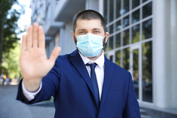 Man in protective face mask showing stop gesture outdoors. Prevent spreading of coronavirus