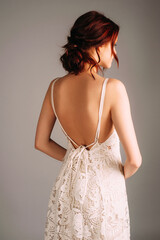 Beautiful portrait of ginger young woman in white summer dress with embroidery details on grey background at studio. Rear view.