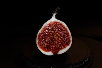 View on isolated raw ripe fig half on black stone background(focus on central fruit)