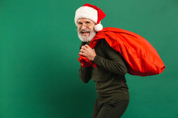 Happy bearded modern Santa Claus holding red bag on the green background