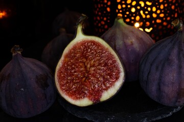 View on isolated raw ripe fig half with group of figs  on black slate stone illuminated by oriental...