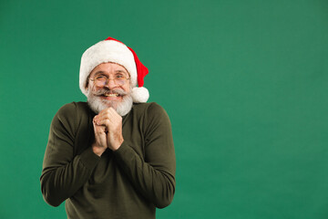 Happy bearded modern Santa Claus holds his hands together and rejoices on a green background