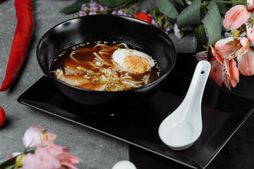 Asian noodle soup, ramen with chicken, tofu, vegetables and egg in black bowl. Slate background