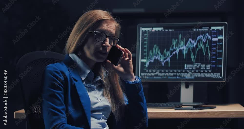 Poster focused business woman in formal wear talking on mobile and looking at computer screen with graphs. 