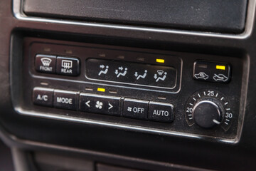 Close-up of the center console on a gray panel inside the car, with climate control and a red emergency button. Setting up and refueling the air conditioner in the workshop.