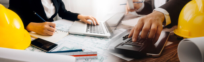 Two colleagues discussing data working and tablet, laptop with on on architectural project at construction site at desk in office