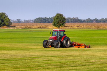 Fototapeta premium Industrial production of lawn grass in rolls. Trimmed field, resistant to mechanical impact and drought of green lawn grass. A tractor with a mower goes through the field, mows and mulches the grass.