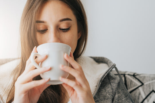 Close Up of Young Woman wearing sweater sipping coffee or tea from white mug in the morning