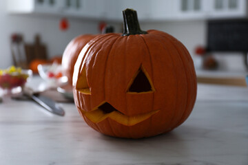 Pumpkin jack o'lantern on white marble table in kitchen. Halloween celebration