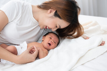 Beautiful asian women mother long hair in the white pajamas. mom kiss at newborn infant with love, while a baby sleeping in her arm with warm, safe, comforted resting on the clean bed.