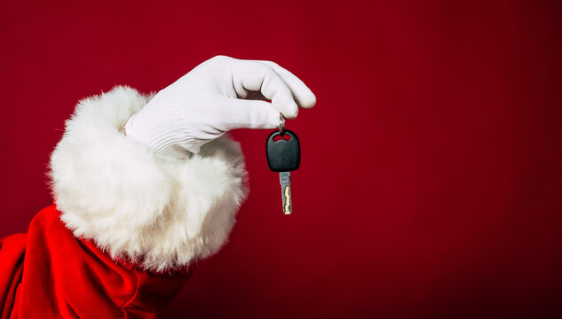 Close up photo of Santa Claus hand in white glove holds key from new apartment or auto isolated on a red background