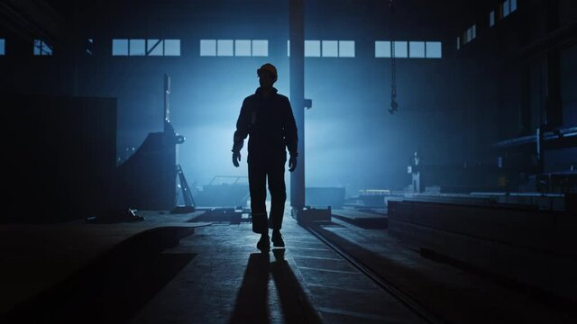 Professional Heavy Industry Engineer/Worker Wearing Uniform, Glasses And Hard Hat In A Steel Factory. Industrial Specialist Walking Towards The Camera In A Dark Metal Construction Manufacture.