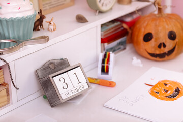 Halloween holiday background with pumpkin and calendar with 31 october on wooden table in schoolgirls room.