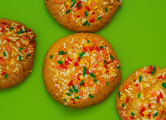 Vanilla cookies with colored sprinkles on a green table 