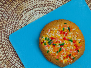 Vanilla cookies with colored sprinkles stacked on a blue plate on a knitted tablecloth.