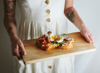 woman in white dress holding a wodden board with beautiful avocado toast with egg and sallad