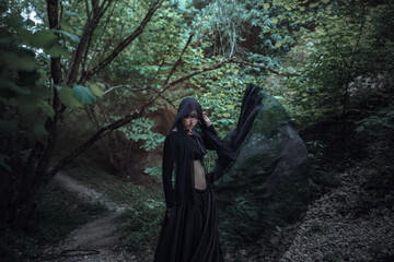 Mysterious sorceress woman witch beautiful black dress walk in gothic forest tree