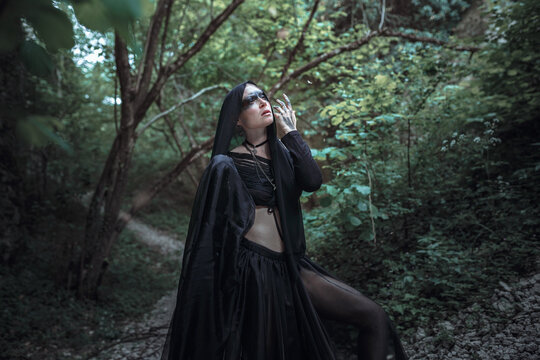 Mysterious sorceress woman witch beautiful black dress walk in gothic forest tree