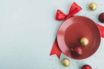 Christmas or New Year party. Plate with red bow and festive decoration on pastel light blue background. Top view, flat lay, copy space