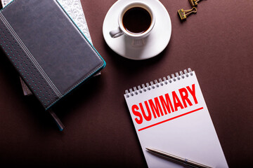 On a brown background, diaries, a white cup of coffee and a notebook with the word SUMMARY