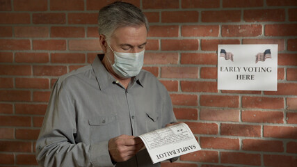 man with a mask during covid-19 looking at a sample voting ballot