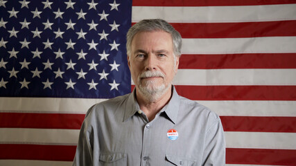 man in front of an american flag wearing an I voted sticker