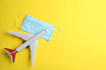 Toy airplane and protective mask on yellow background, flat lay with space for text. Travelling...