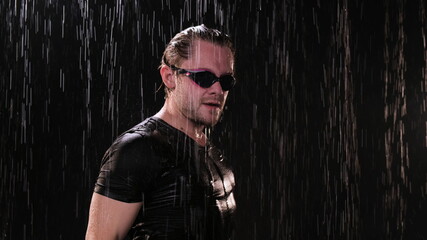 Funny man in black t-shirt under rain in night on black background put on swimming glasses