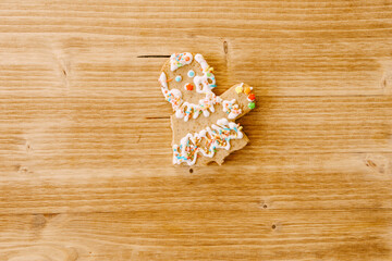 Partially eaten gingerbread man. Gingerbread in the shape of a man - without legs and arms. On a light wood texture.