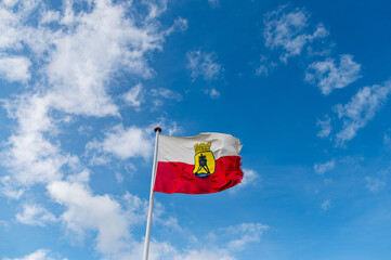 Flag of the coast town Cuxhaven showing the city's symbol Kugelbake flying in the wind in front of a bright blue sky with white clouds.