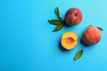 Fresh ripe peaches and green leaves on light blue background, flat lay. Space for text