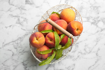 Fresh sweet peaches in metal basket on white marble table, top view