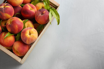 Fresh sweet peaches in wooden crate on light table, top view. Space for text