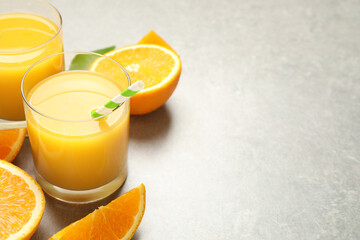 Glasses of orange juice and fresh fruits on light grey table, closeup. Space for text