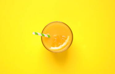 Glass of orange juice on yellow background, top view
