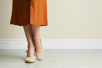 Woman wearing stylish shoes near beige wall indoors, closeup. Space for text