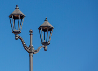 Old street lamp close-up against the blue sky.